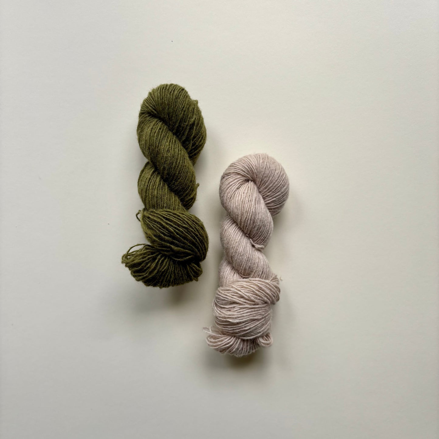 Two skeins of yarn, one green and one beige, on a light gray background
