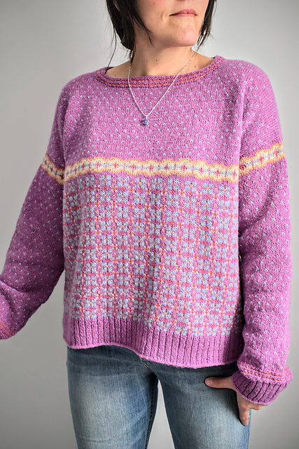 Person wearing a purple sweater with a patterned design on a plain background