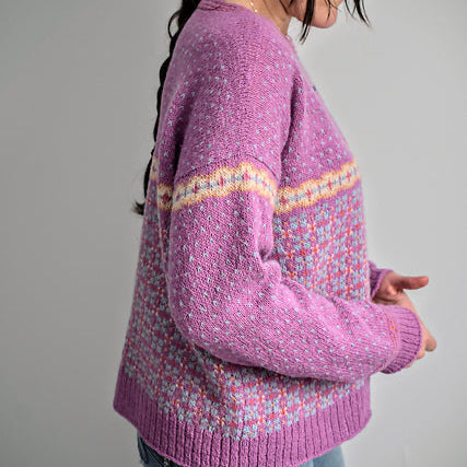 Woman wearing a purple sweater with a patterned design on a plain background
