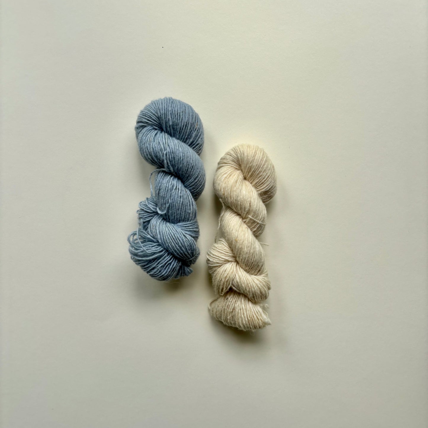 Two skeins of yarn, one blue and one white, on a light grey background