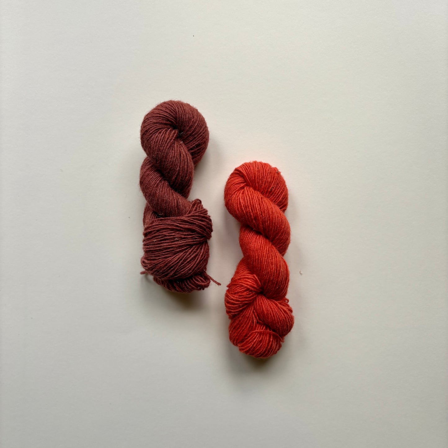 Two skeins of yarn, one brown and one red, on a light gray background.